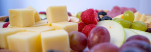 a close up scene of blocks of cheddar cheese and grapes and raspberries